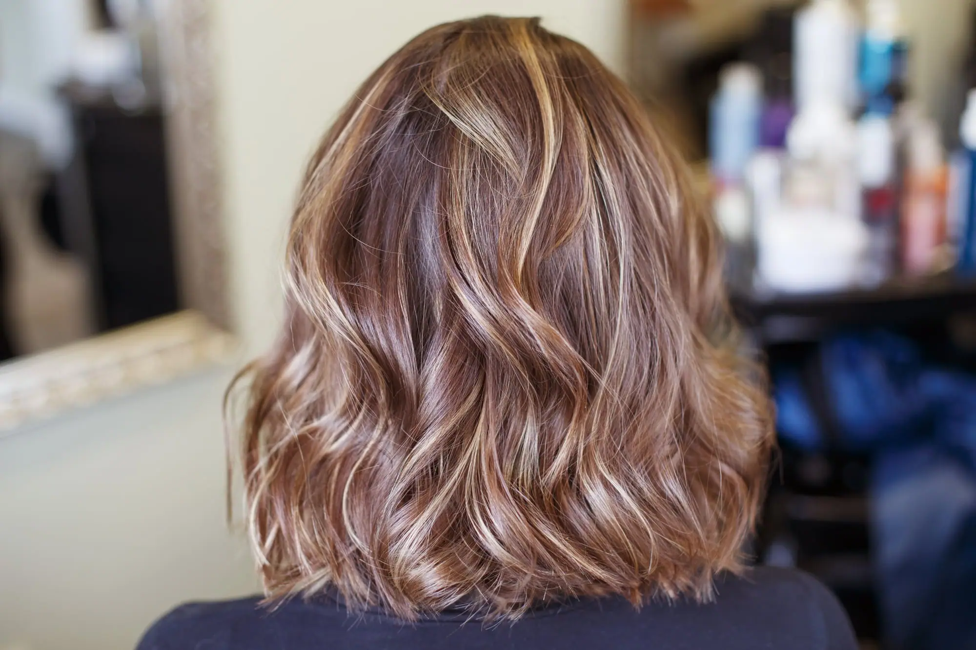 Melena castaña ondulada con mechas rubias suaves, vista de espaldas en el salón