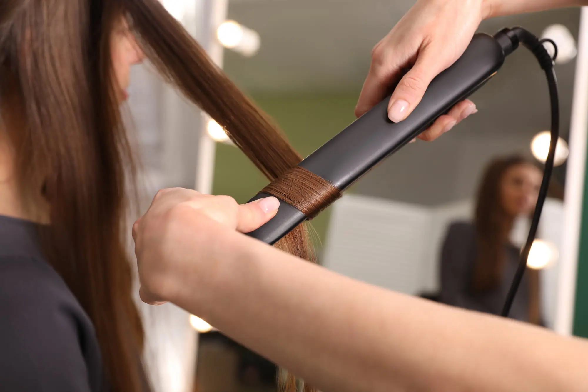 Peluquera alisando con plancha la melena castaña y larga de una clienta
