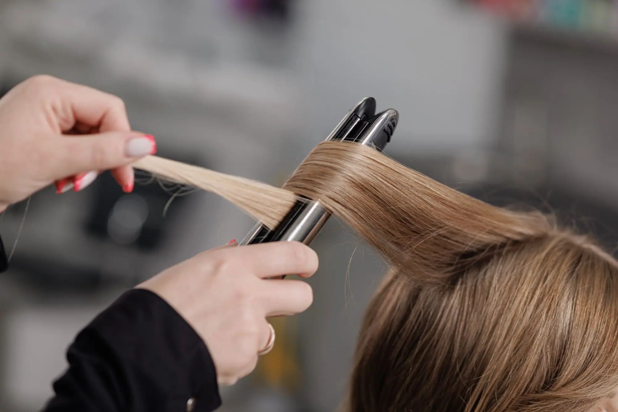 Peluquera pasando la plancha por un mechón de pelo rubio oscuro